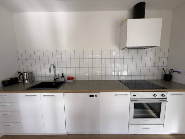 Una cucina moderna con mobili bianchi, un lavello nero, forno integrato e schienale piastrellato.