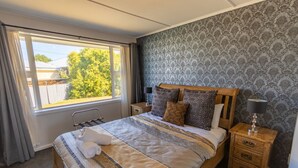 Una cama bien hecha con ropa de cama estampada, un cabecero de madera y una mesita de noche con una lámpara.