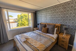 A neatly made bed with patterned bedding, a wooden headboard, and a bedside table with a lamp. - Fantastic Family Home on Fraser -FREE WIFI -TWIZEL (Twizel)