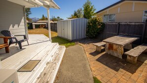 Un patio con una terraza de madera, un cobertizo metálico y una mesa de picnic con bancos.