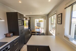 Een moderne keuken met donkerhouten kasten, een wit aanrecht en een eethoek met tafel en stoelen.