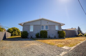 A single-story house with a gabled roof, a front porch, and a gravel driveway. - Fantastic Family Home on Fraser -FREE WIFI -TWIZEL (Twizel)