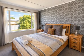 A neatly made bed with a patterned bedspread, two bedside tables with lamps, and a window with curtains.