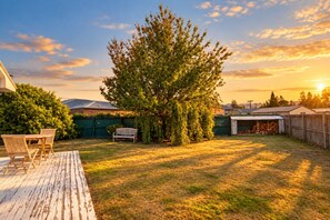 Un jardin avec une terrasse en bois, un banc, un arbre et un abri de jardin.
