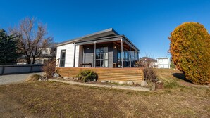Ett envåningshus med en inglasad veranda, en liten trädgård framför huset med ett trädäck och ett stort träd med höstfärgade löv.