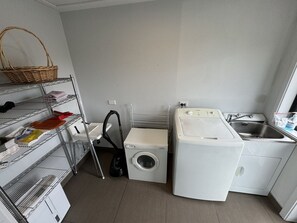 A compact laundry room with a washing machine, dryer, and shelves with cleaning supplies. - Big Sky, Big View - Family friendly and close to Mt Cook, FREE WIFI (Twizel)