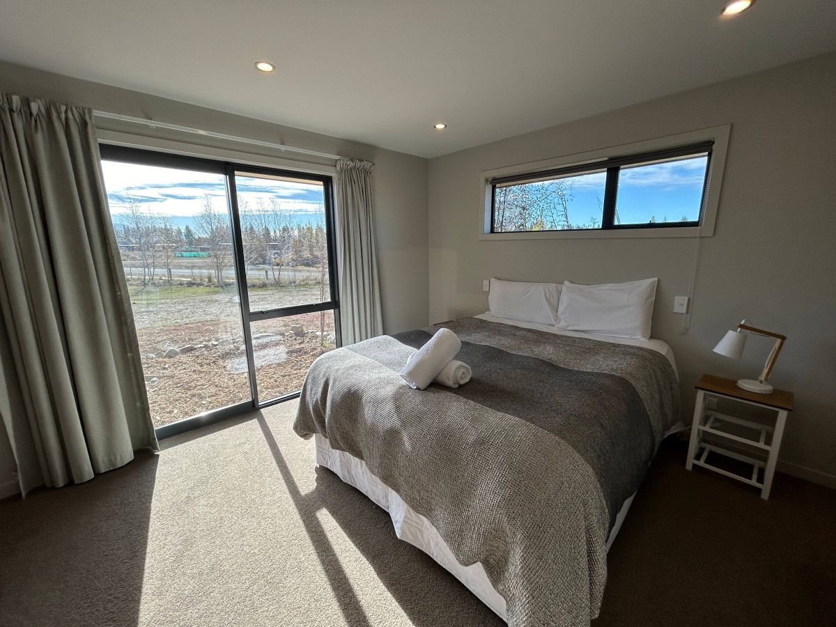 A bedroom with a large bed, a nightstand, a window, and a view of the outdoors.