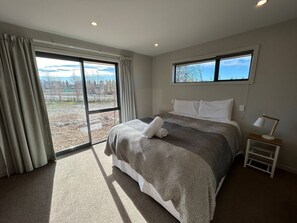 A bedroom with a large bed, a nightstand, a window, and a view of the outdoors. - Big Sky, Big View - Family friendly and close to Mt Cook, FREE WIFI (Twizel)