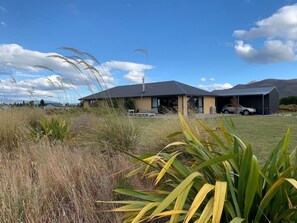 A modern house with a large garage, surrounded by tall grass and a clear blue sky. - Big Sky, Big View - Family friendly and close to Mt Cook, FREE WIFI (Twizel)