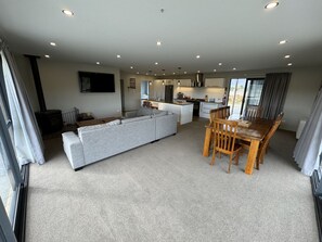 A modern living room with a grey sofa, wooden dining table, and a kitchen area in the background. - Big Sky, Big View - Family friendly and close to Mt Cook, FREE WIFI (Twizel)