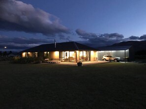 A modern house with a large garage, a car parked inside, and a well-lit exterior at dusk. - Big Sky, Big View - Family friendly and close to Mt Cook, FREE WIFI (Twizel)