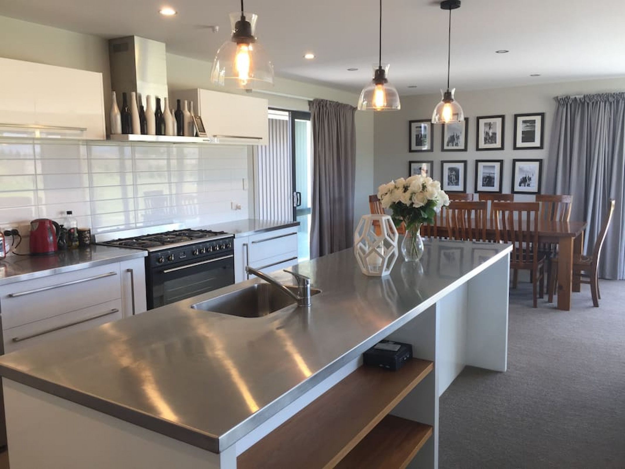 A modern kitchen with stainless steel appliances, a central island, pendant lighting, and a dining area with a wooden table and chairs.