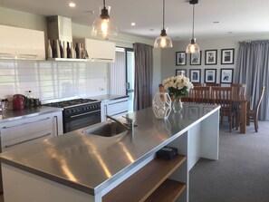 A modern kitchen with stainless steel appliances, a central island, pendant lighting, and a dining area with a wooden table and chairs. - Big Sky, Big View - Family friendly and close to Mt Cook, FREE WIFI (Twizel)