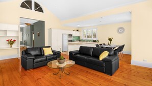 A spacious living room with two black leather sofas, a glass coffee table, and a dining area with a table and chairs. - Adelaide Style Accommodation-City-Beach (Everard Park)