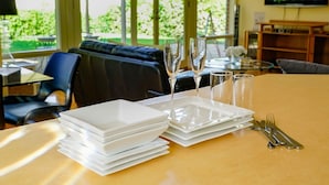 A dining table set with white plates, glasses, and cutlery, with a view of greenery outside through large windows. - Adelaide Style Accommodation-City-Beach (Everard Park)