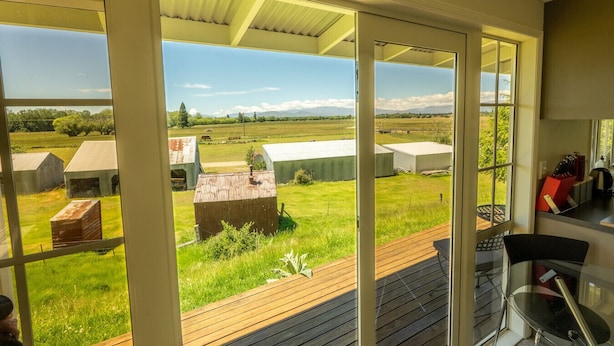 Habitación con amplias puertas correderas de vidrio que dan a una terraza, con vistas a una zona verde y edificios agrícolas.