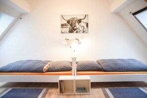 Un dormitorio tipo loft con techo inclinado, una cama con almohadas estampadas, una lámpara de pared y un cuadro con la imagen de un toro.