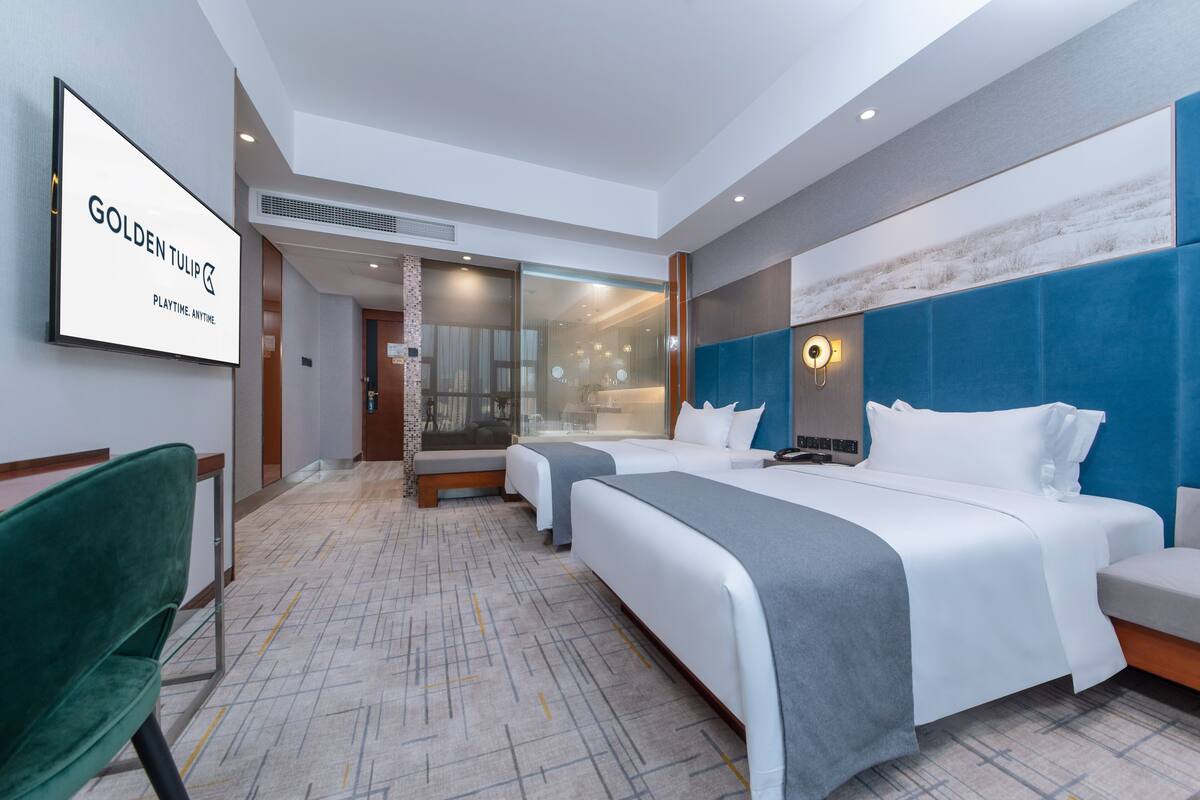 A hotel room with a large bed, two bedside tables, a green chair, and a large mirror.