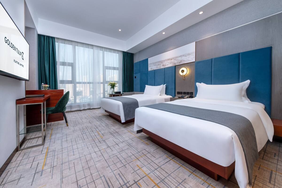 A hotel room with two beds, a desk, and a TV.