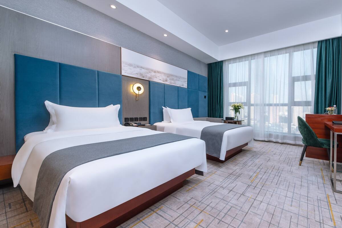 A hotel room with two beds, a desk, and a view of the city.