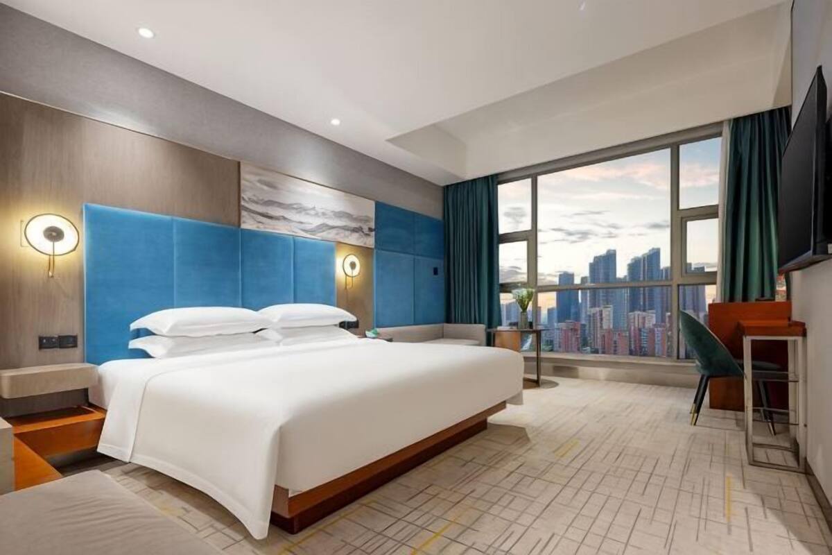 A hotel room with a large bed, a city view, a desk, and a chair.
