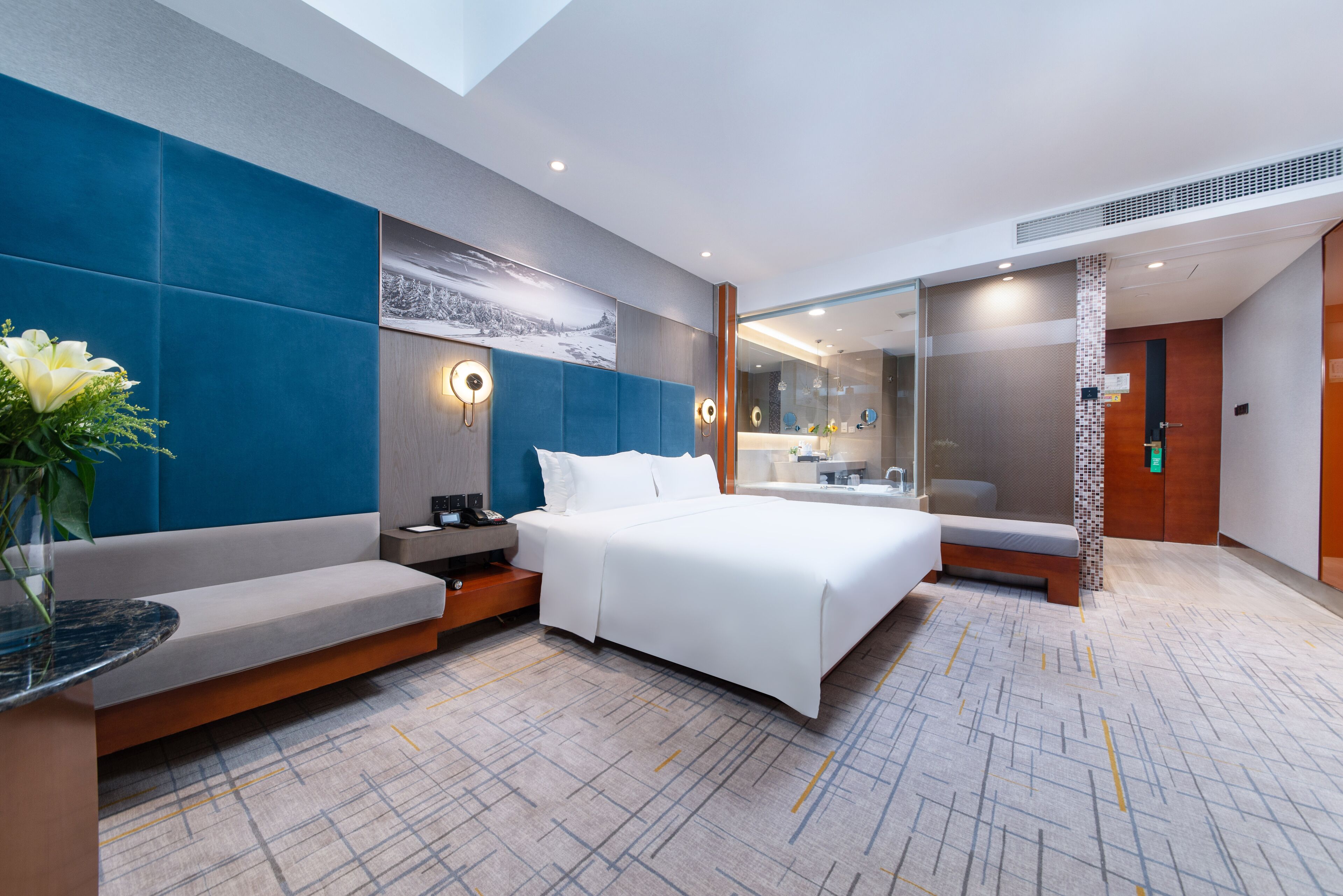 A modern hotel room with a large bed, a seating area, a bathroom, and a view of the city.