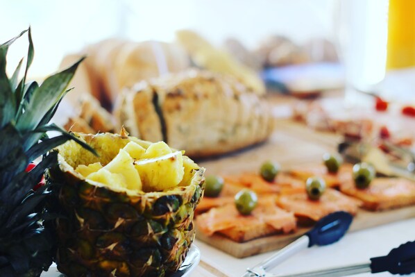 Une table avec un ananas, des fruits coupés en tranches et une planche de fromages accompagnée d’olives.