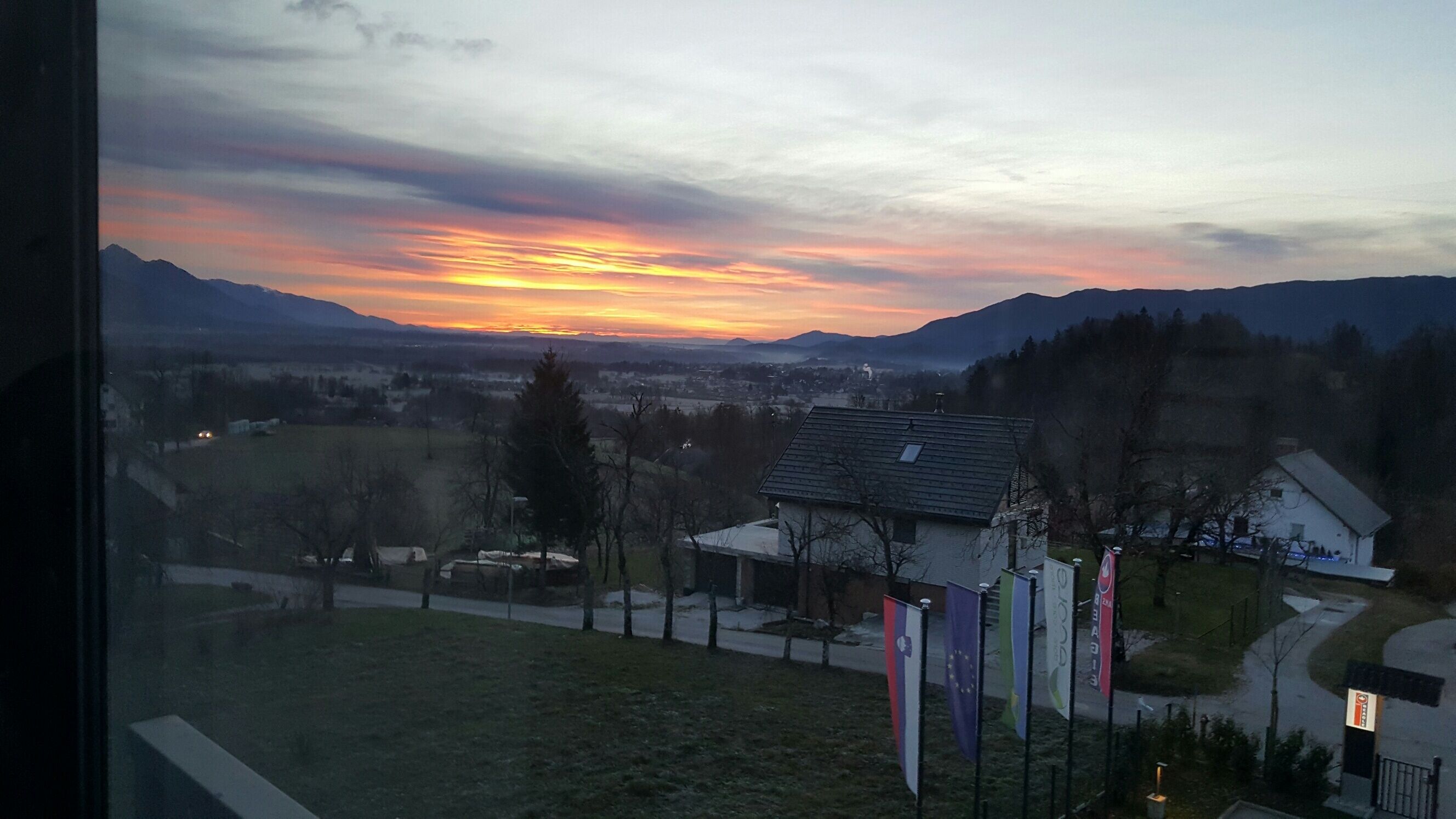 Vista de un pueblo con el atardecer sobre montañas, casas y banderas.