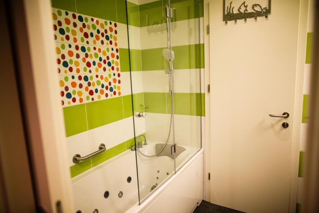 Une salle de bain avec une douche à parois de verre, une baignoire blanche et un mur à rayures vertes et blanches.