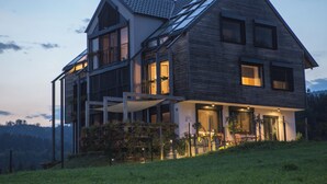 A modern two-story house with a sloped roof, large windows, and a well-lit exterior. - eco boutique hotel A.M.S. Beagle Bled (Gorje)