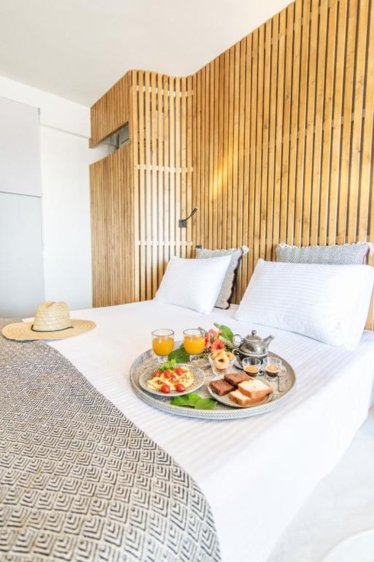 Una cama bien hecha con una bandeja de desayuno que incluye tostadas, fruta y jugo.