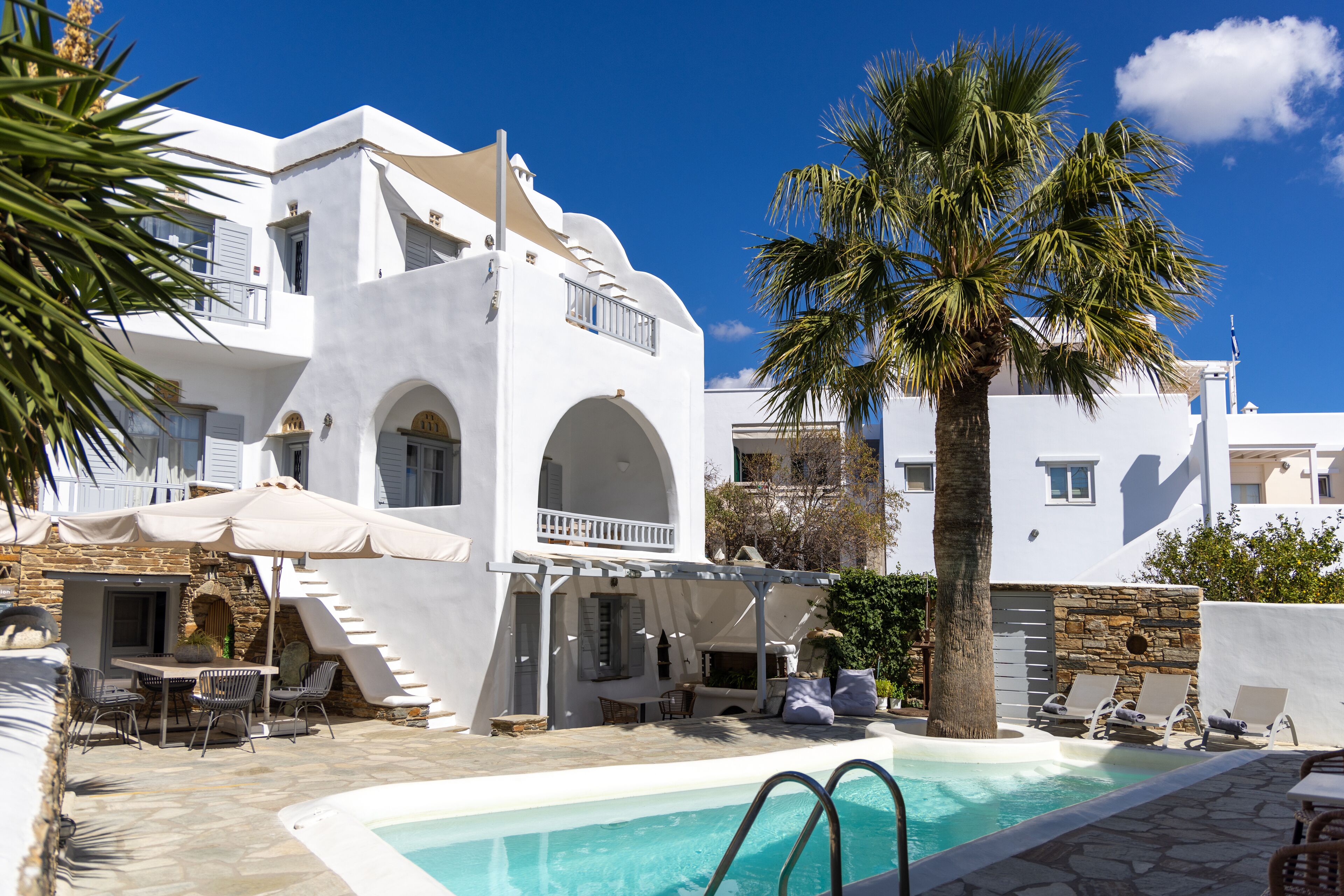 Un edificio blanco con piscina, mesas al aire libre y una palmera.