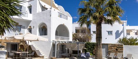 Un edificio blanco con piscina, mesas al aire libre y una palmera.