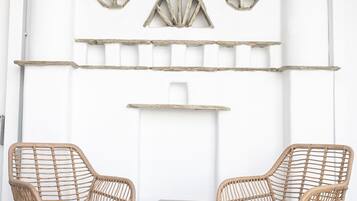 Duas cadeiras de vime com almofadas pretas, uma pequena mesa de concreto e uma parede decorativa com padrões geométricos e elementos de madeira.
