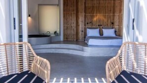 Ein modernes Schlafzimmer mit einem großen Bett, einer kleinen Sitzecke mit Tisch und Stühlen und Blick ins Zimmerinnere.