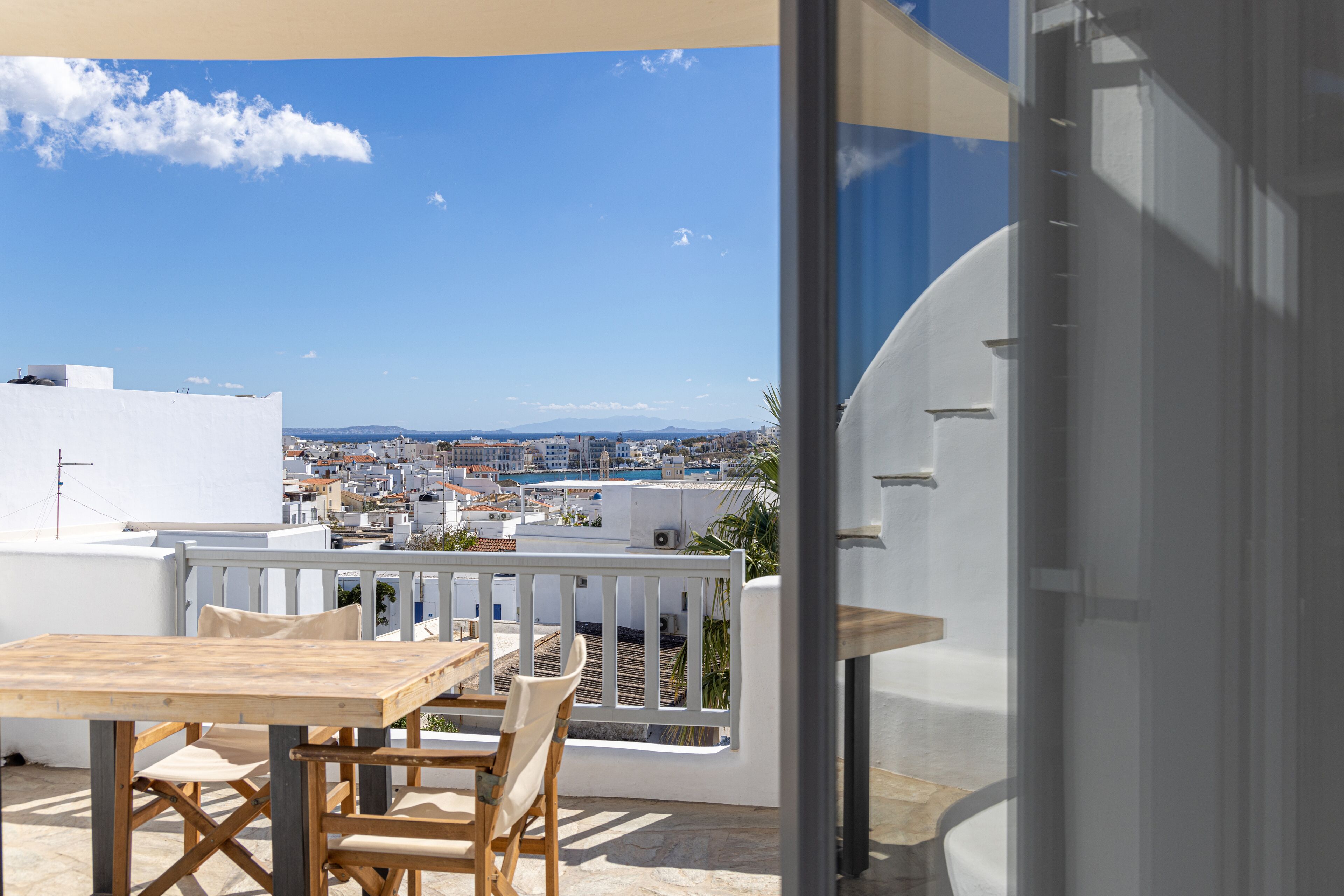 A balcony with a wooden table and chairs, offering a view of a cityscape and distant mountains.