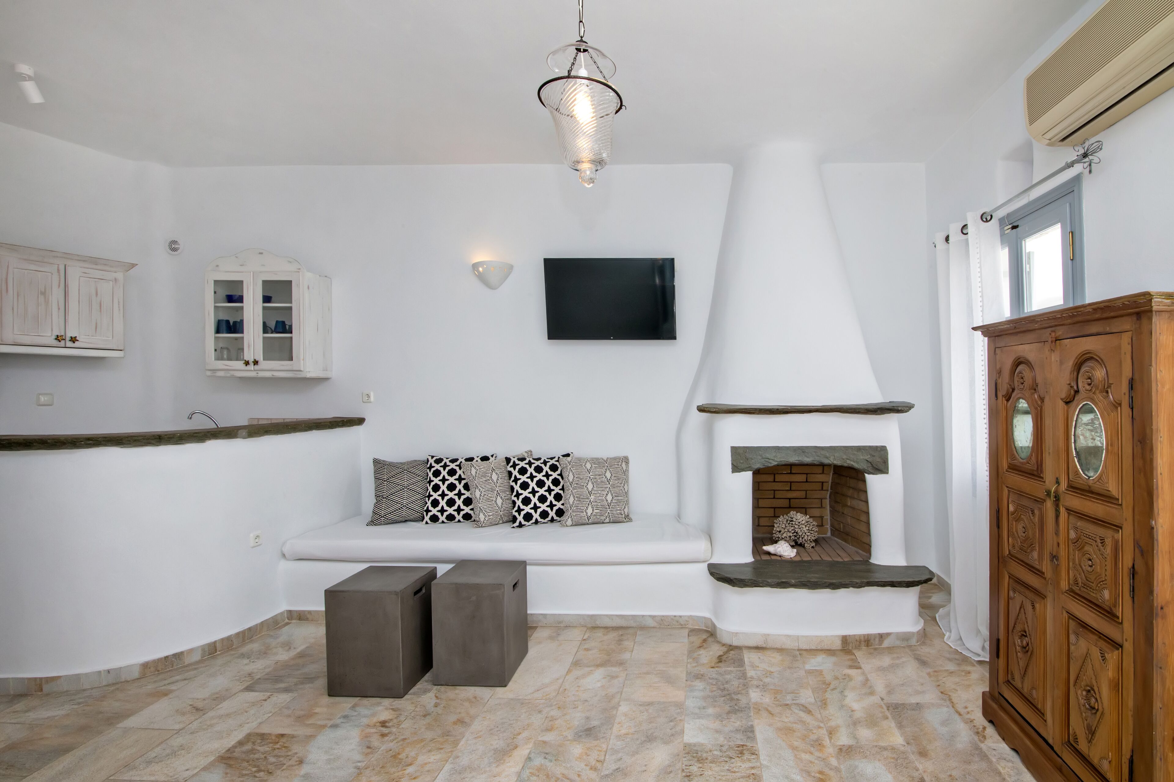 A modern kitchen with white cabinetry, a built-in seating area, a flat-screen TV, and a stone fireplace.