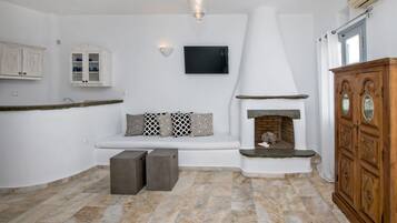 A modern kitchen with white cabinetry, a built-in seating area, a flat-screen TV, and a stone fireplace.