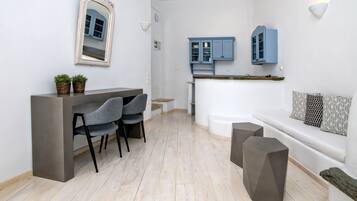 A modern kitchen with blue cabinets, a dining area with a grey chair, and a white sofa with patterned cushions.