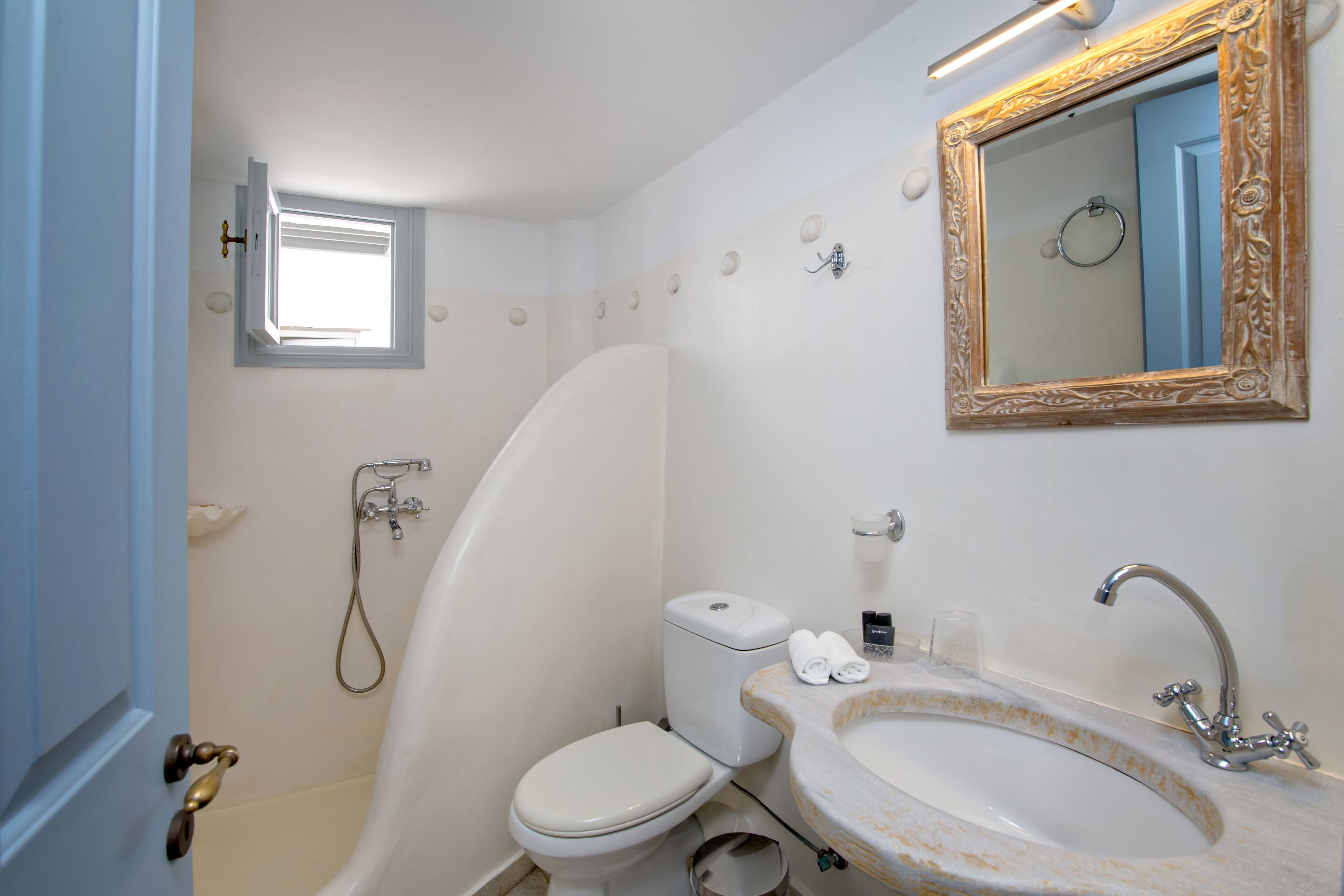 A bathroom with a toilet, sink, shower, and a small window.