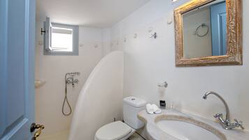 A bathroom with a toilet, sink, shower, and a small window.