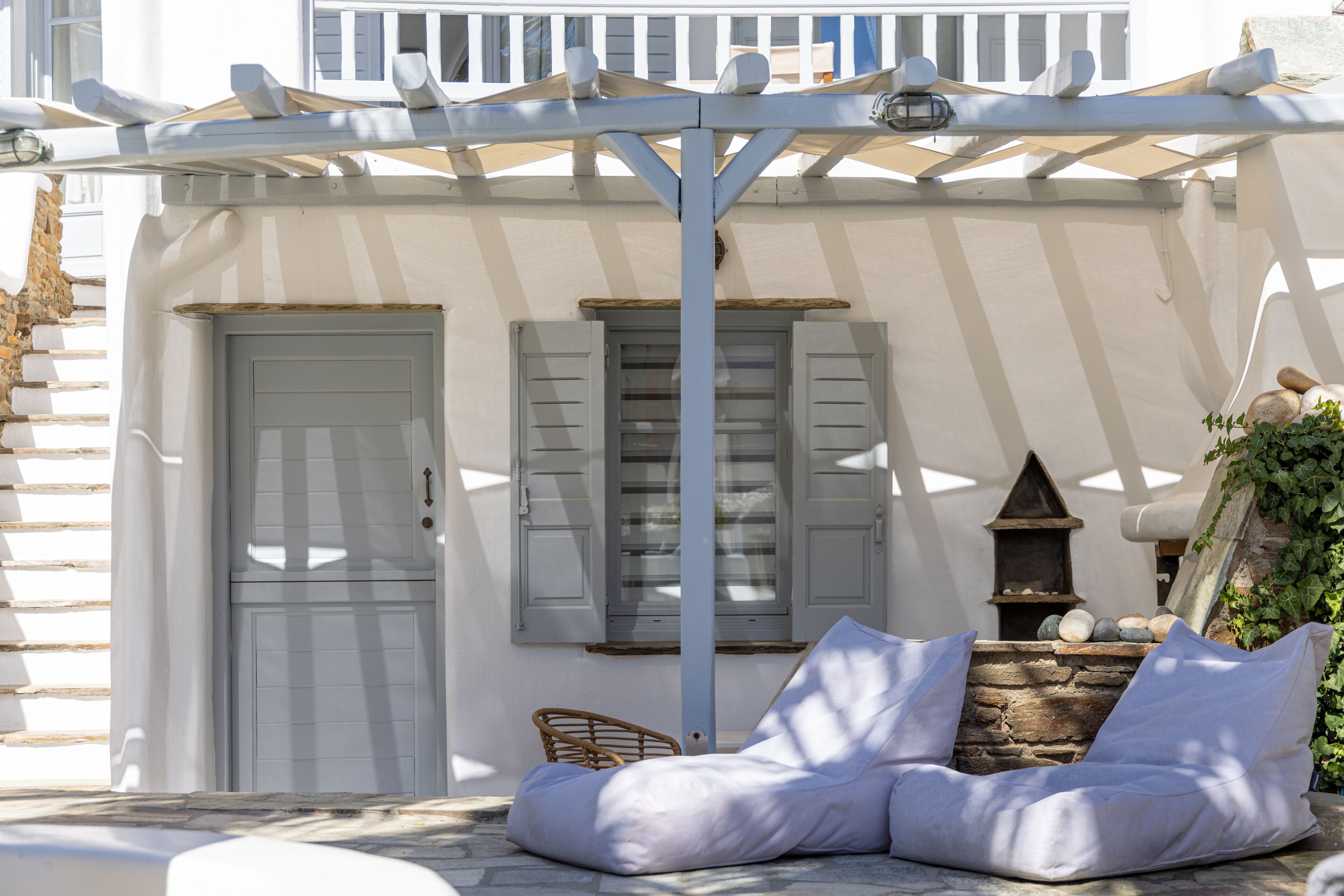 A white building with a stone wall, a wooden door, and a white bench with cushions.