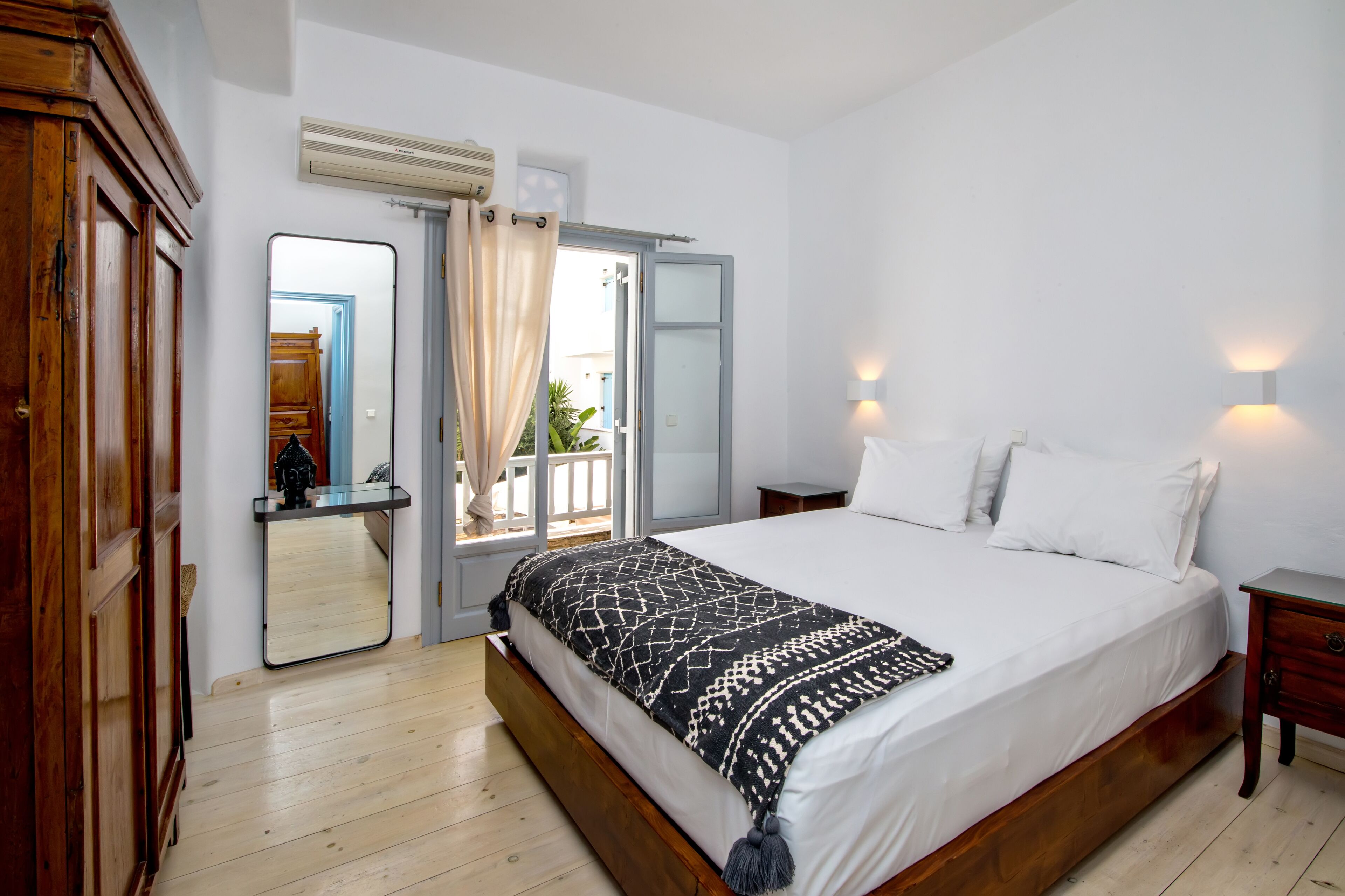Un dormitorio con cama de madera, ropa de cama blanca, un espejo y una mesita de noche.