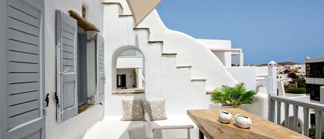 A white building with a wooden table and chairs, a stone floor, and a view of the city.
