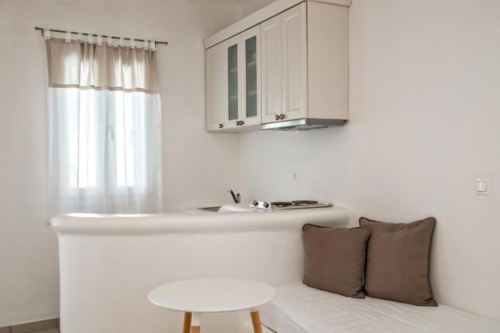 A compact kitchenette with a sink, stove, and cabinets. There is a small round table and a sofa with cushions.