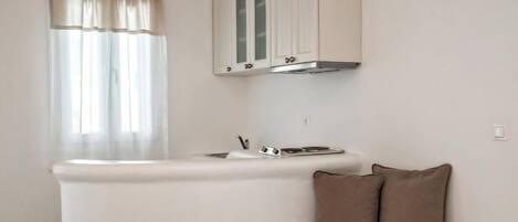 A compact kitchenette with a sink, stove, and cabinets. There is a small round table and a sofa with cushions.