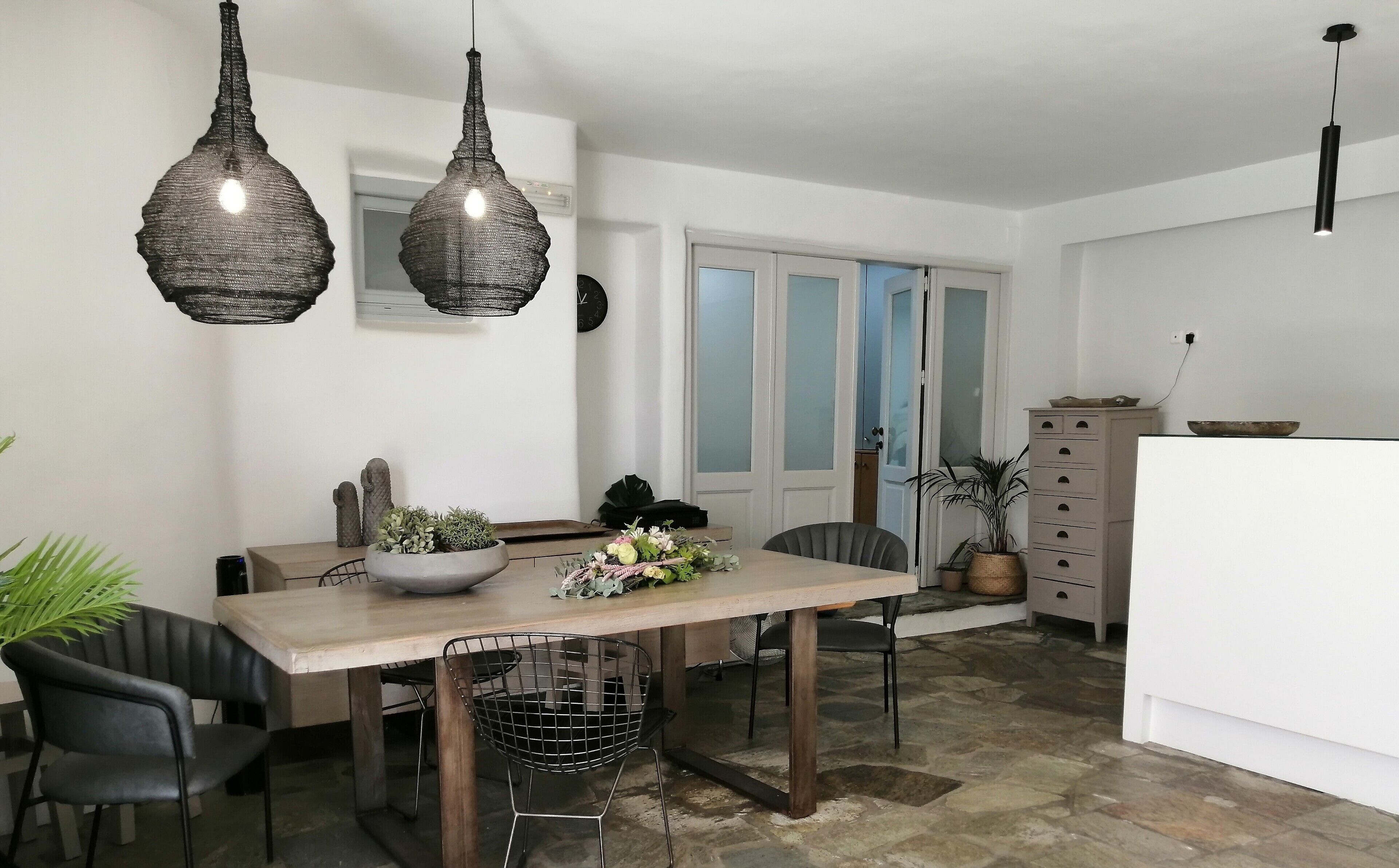 Comedor con mesa de madera, dos sillas, un cuenco de flores y lámparas colgantes.