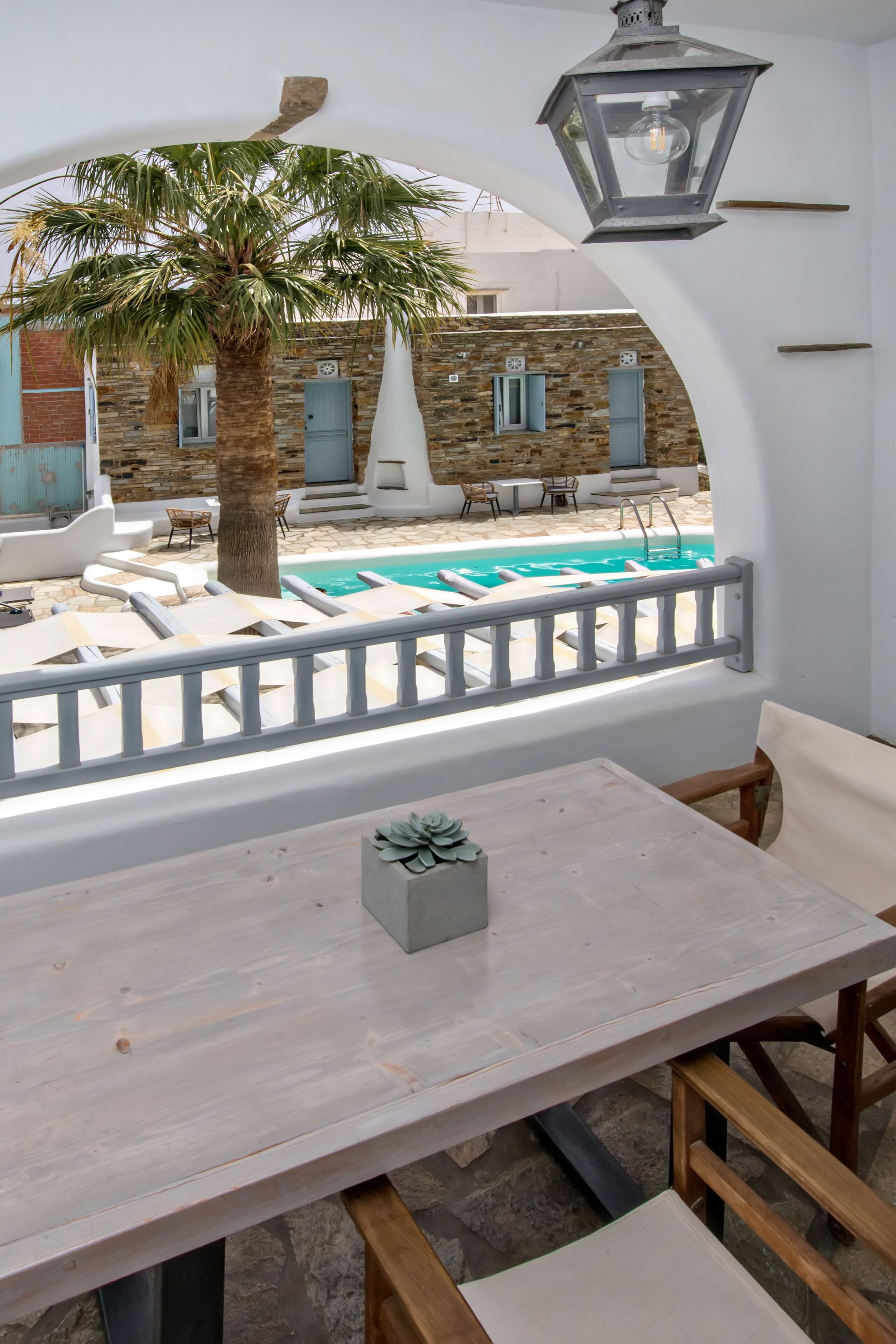 Un área junto a la piscina con una mesa y sillas, una palmera y un edificio de piedra al fondo.