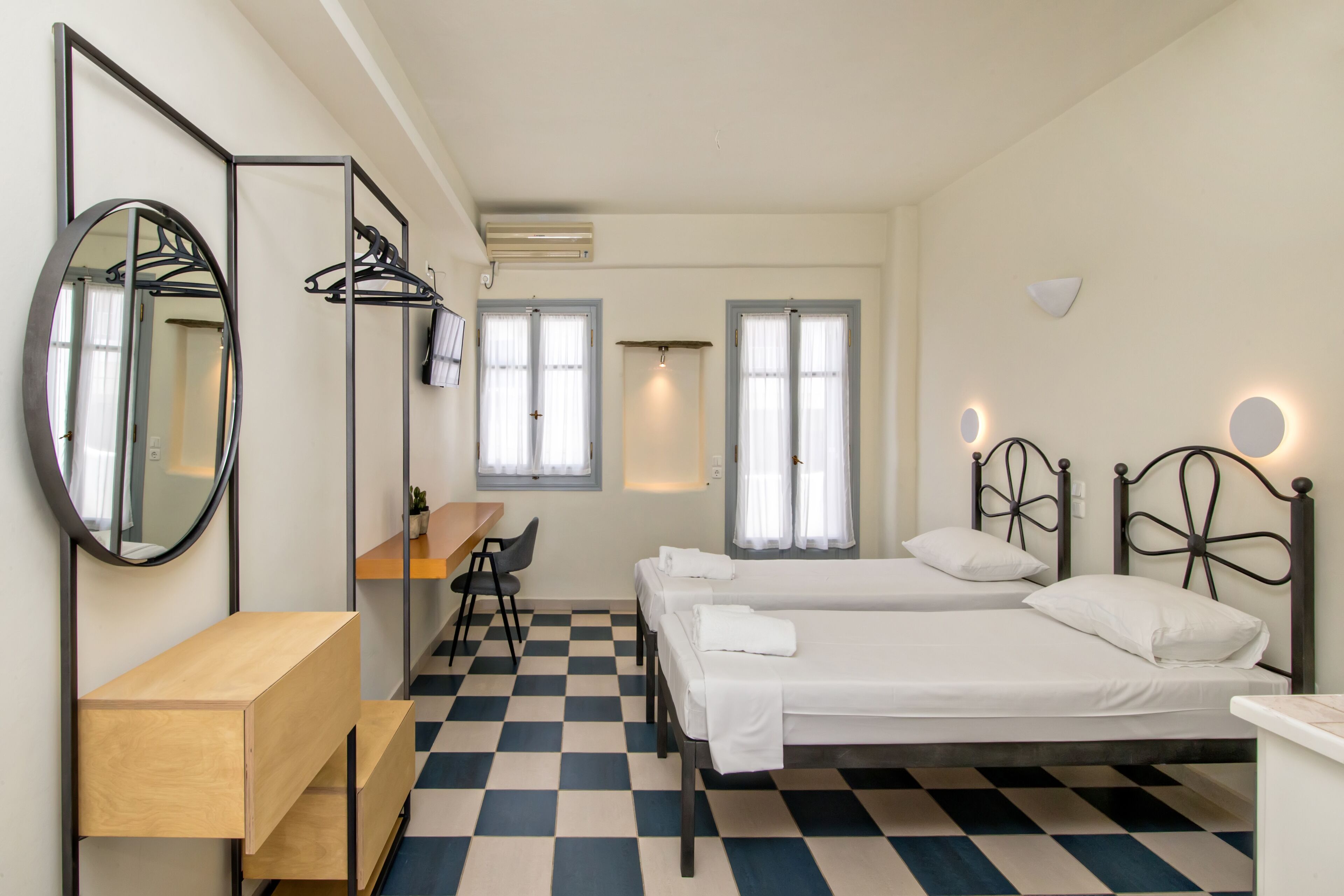 Quarto de hotel com duas camas de solteiro, uma escrivaninha, uma cadeira e um espelho.