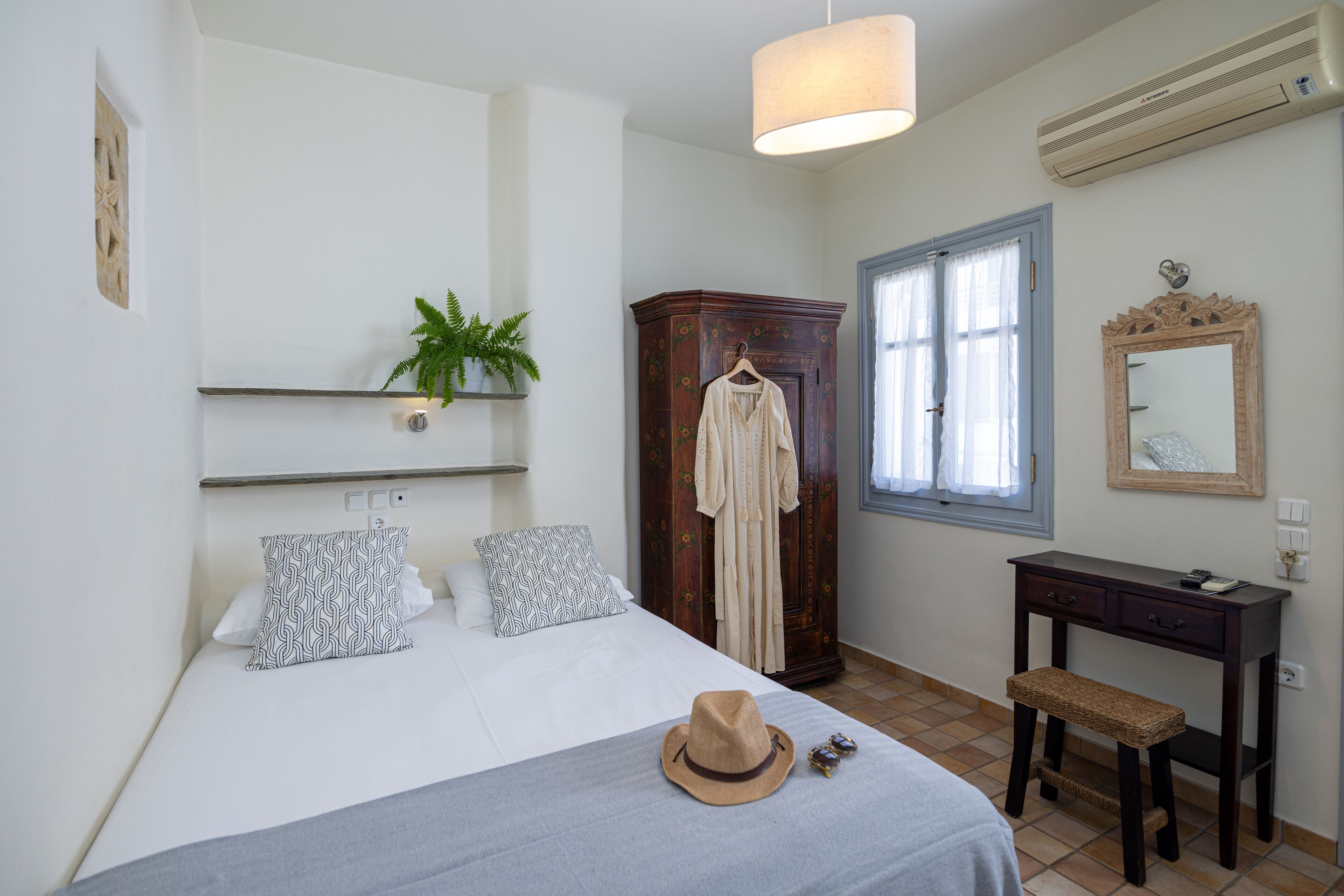 Un dormitorio con cama, armario, escritorio y una planta colgante.
